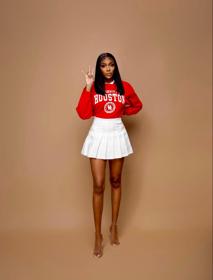 a woman in a red sweatshirt and white skirt posing for the camera with her hand up