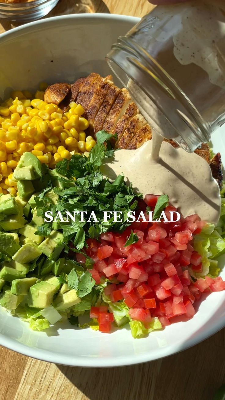 a bowl filled with salad and dressing on top of a wooden table next to a glass bottle