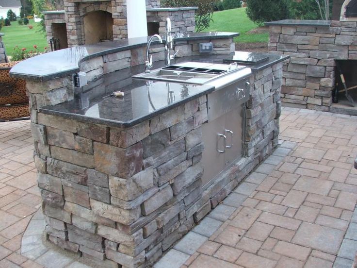 an outdoor kitchen is built into the side of a brick wall and features stainless steel appliances