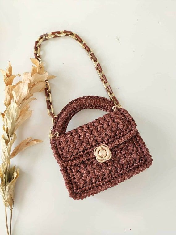 a crocheted brown purse sitting on top of a white table next to a plant