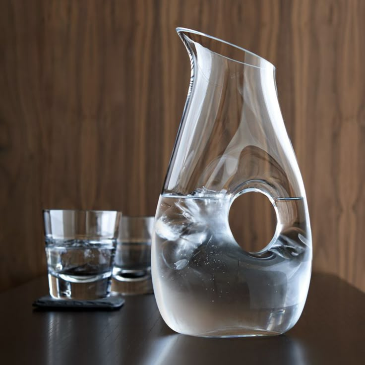 a clear glass vase sitting on top of a table next to two glasses and a phone