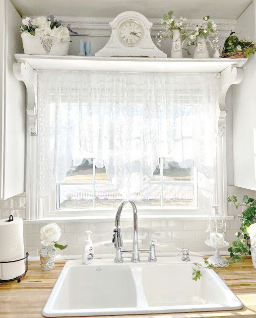 a white kitchen sink sitting under a window next to a counter top with flowers on it