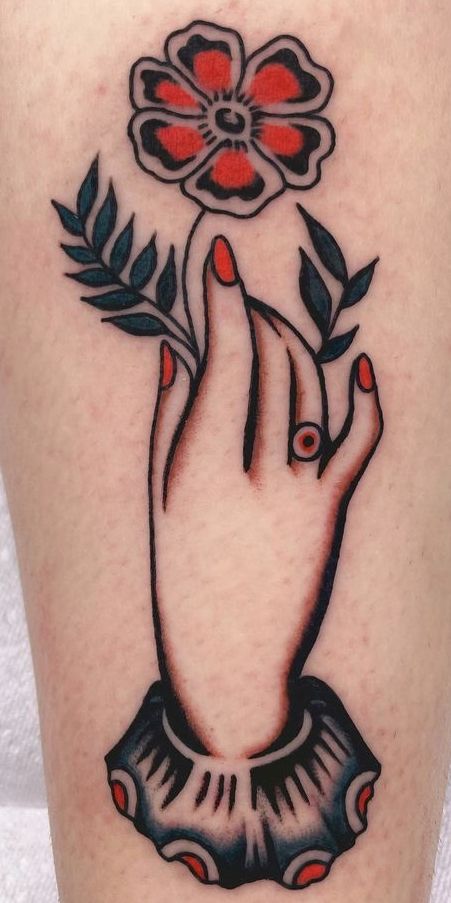 a woman's hand holding a flower tattoo on her right thigh with red and black accents