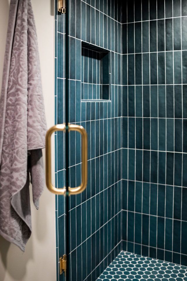 a blue tiled shower with gold handles and hand towels hanging on the wall next to it