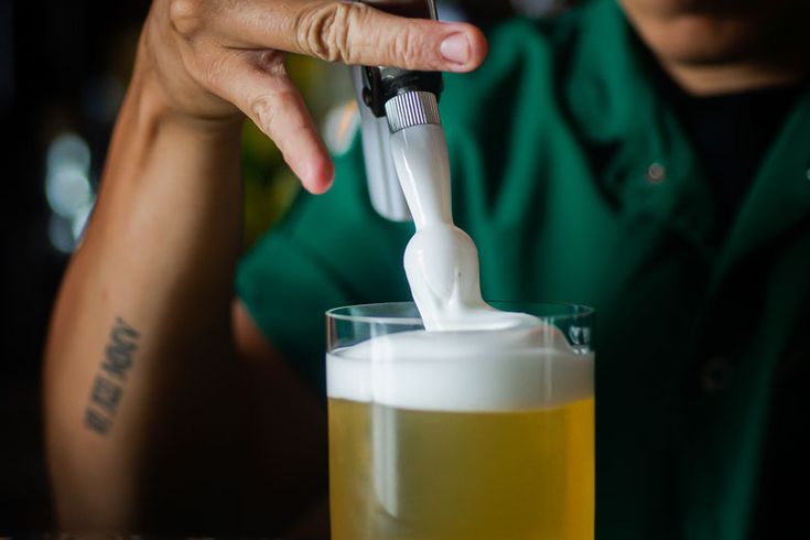 a person is holding a toothbrush in a glass of beer while another person watches