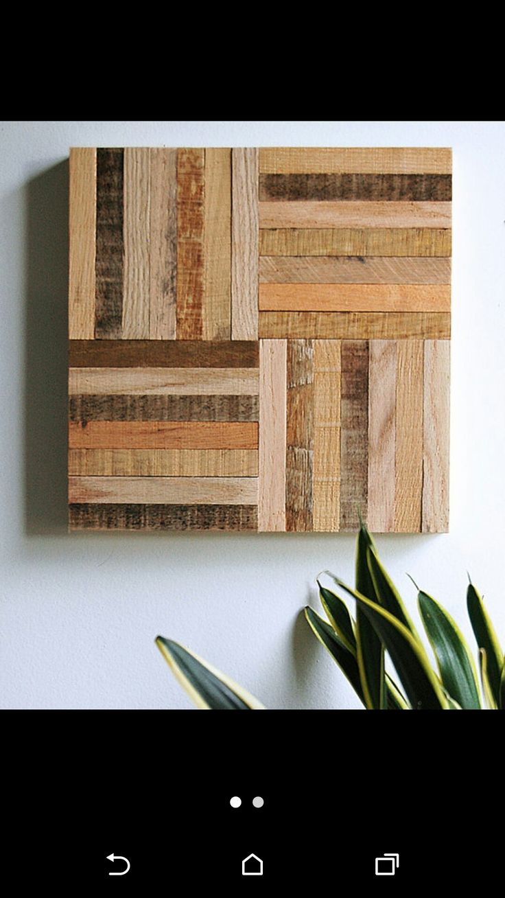 a wooden wall hanging on the side of a white wall next to a potted plant