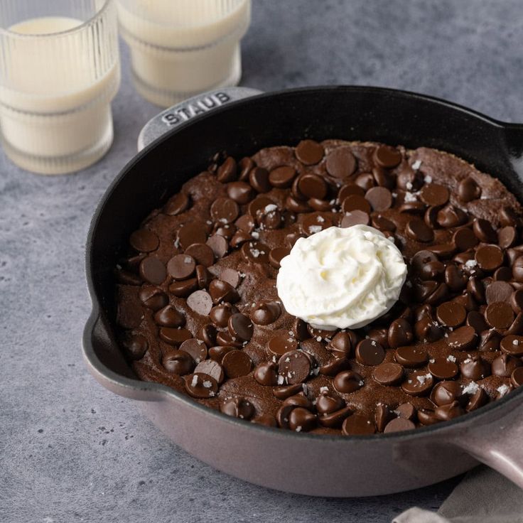 a chocolate cake in a pan with whipped cream on top and two glasses of milk next to it