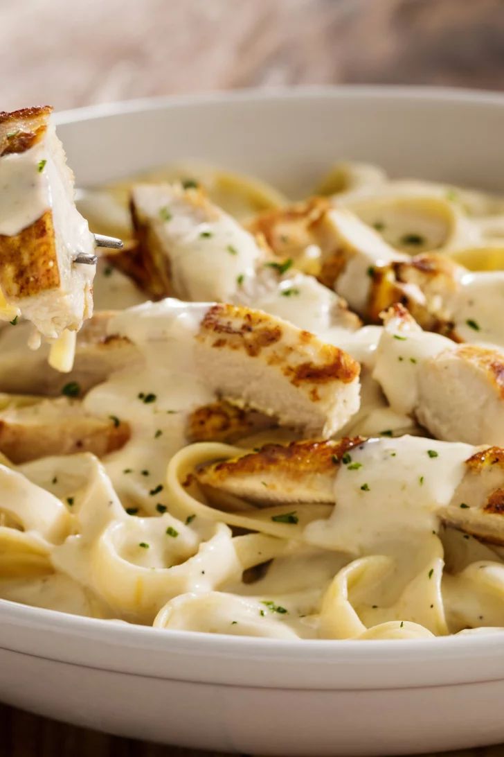 a fork is being lifted from a bowl of pasta with chicken and parmesan cheese