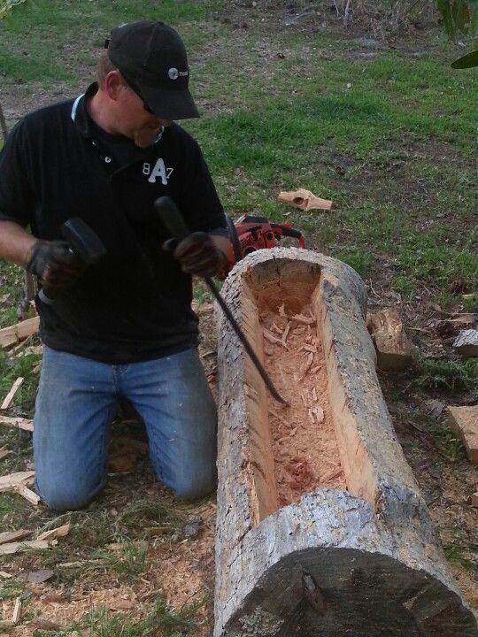 a man in black shirt and hat working on a piece of wood with an ax