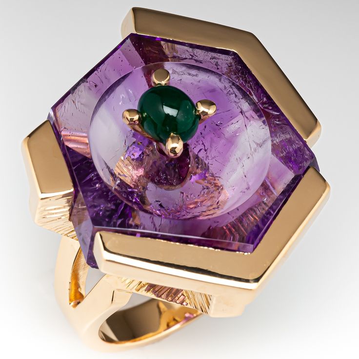 This spectacular vintage cocktail ring is accented with hexagonal shaped fantasy cut natural amethyst set into an abstract semi-bezel/prong setting. The top of the amethyst features a flat top with a carved bowl in the middle and accented with one (1) oval cabochon cut natural emerald set into a four-prong head. The ring measures 31.9mm at the top, rises 15.7mm above the finger, tapering to 4.4mm wide and 2.0mm thick at the base of the shank. This ring is currently a size 6.25 and shows only lig Big Stone Rings, Vintage Eternity Band, Stone Rings For Women, Carved Bowl, Amethyst Cocktail Ring, Amethyst Ring Vintage, Emerald Set, Big Stone Ring, Amethyst Set