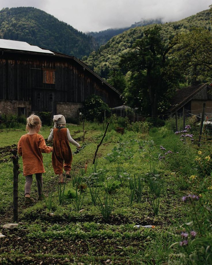 two children are walking through the grass in front of a barn