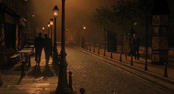 people walking down the street at night in an old city with lights on and fog