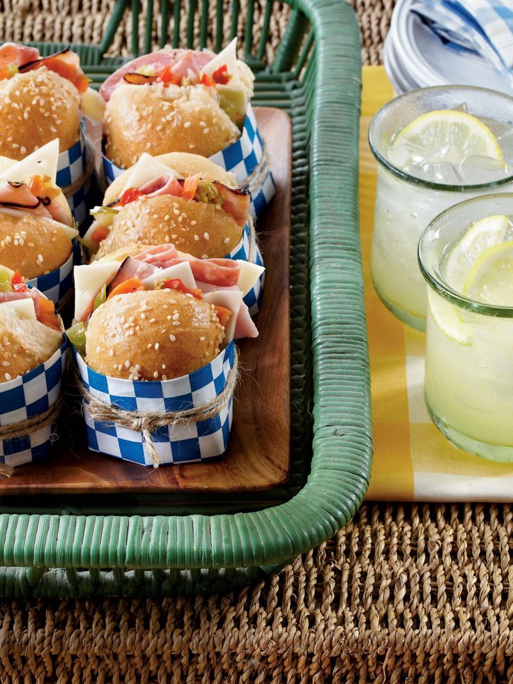 small sandwiches are arranged in baskets on a tray next to some lemonades and glasses