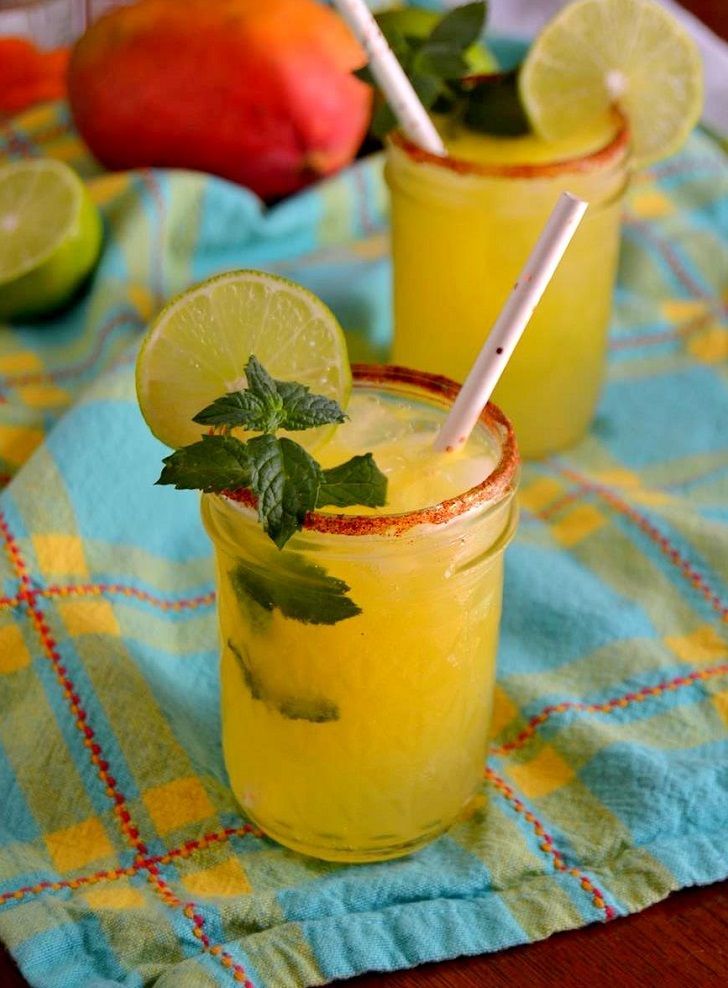 two glasses filled with lemonade, lime and mint on a blue towel next to fruit