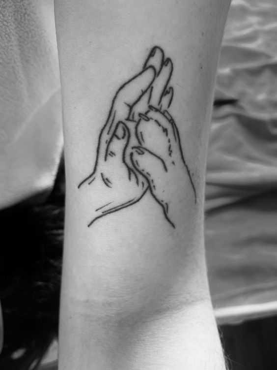 two hands holding each other in the middle of a tattoo on someone's arm