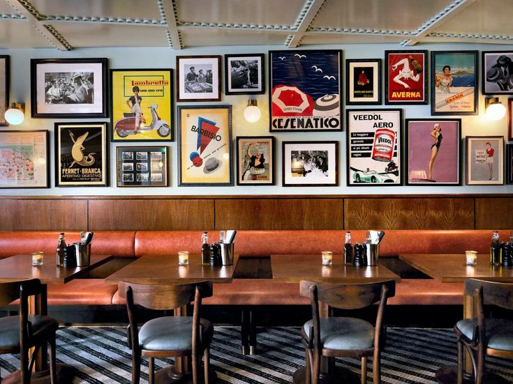 an empty restaurant with tables and chairs in front of a wall full of framed pictures