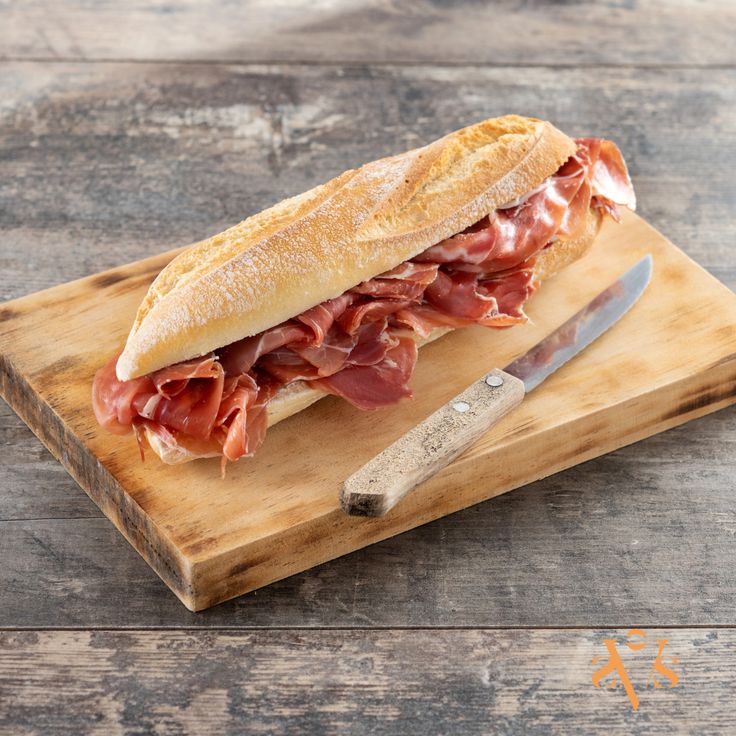 a ham and cheese sub sandwich on a cutting board with a knife next to it