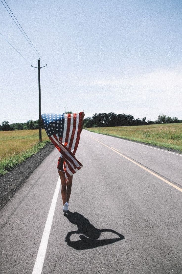 a person carrying an american flag down the road