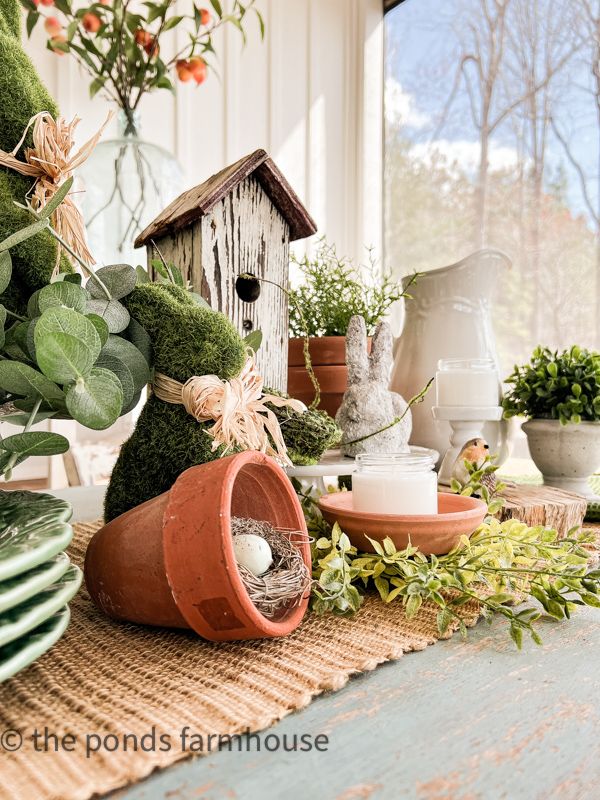 a bird house sitting on top of a table next to potted plants and plates