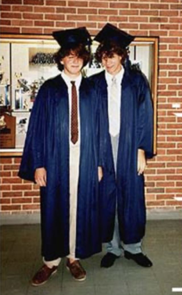 two men in graduation gowns standing next to each other with their arms around each other