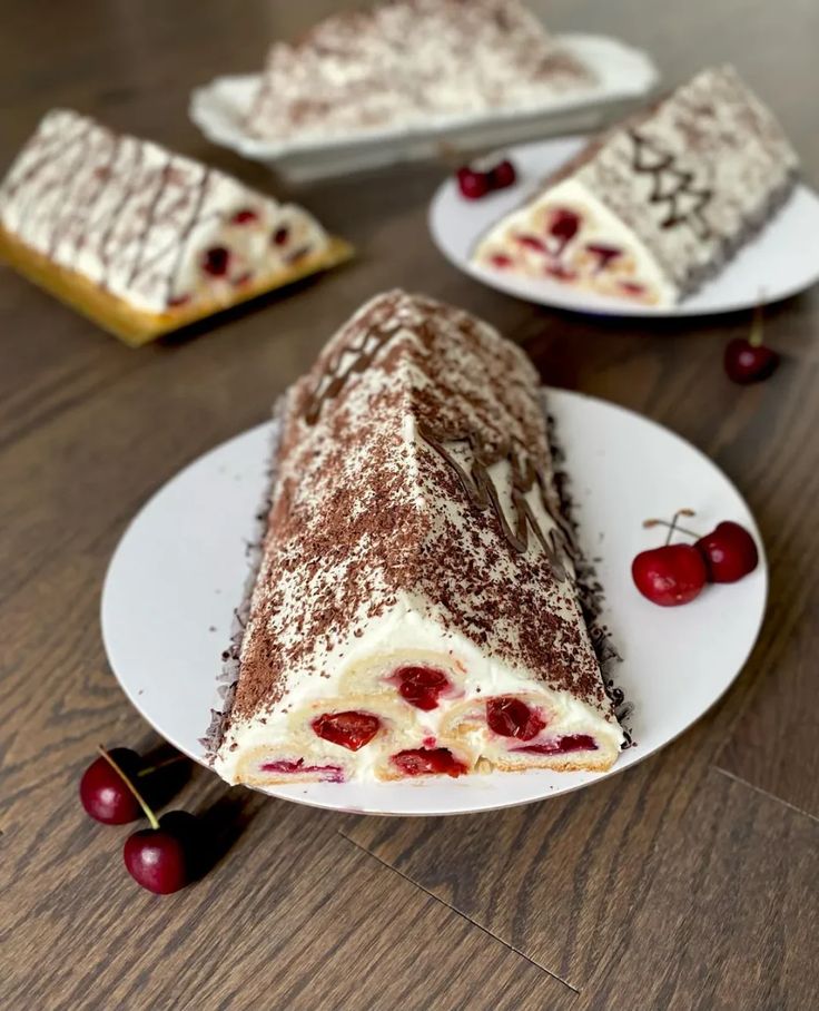 a piece of cake sitting on top of a white plate next to two cherries