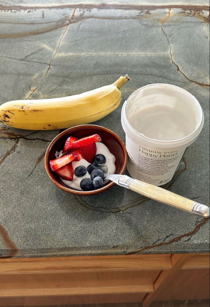 a bowl of fruit, yogurt and a banana sitting on a counter top