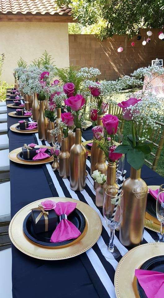 the table is set with pink flowers and gold vases on black and white stripes