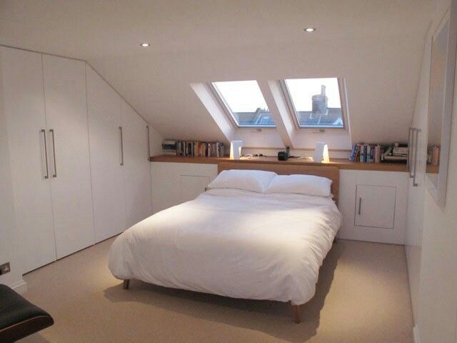 a bed sitting under two windows in a bedroom next to a book shelf and desk