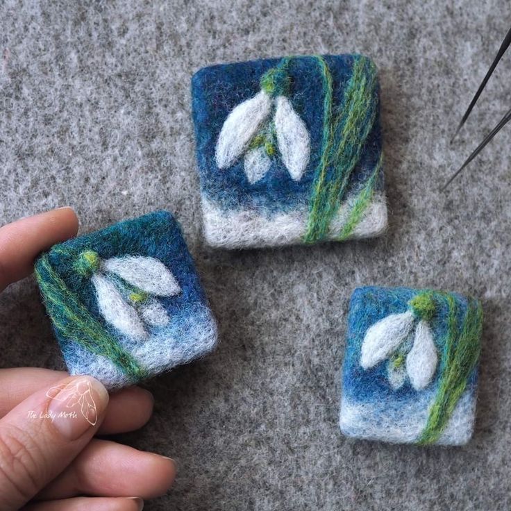 three small pieces of felt with white flowers on them are being held by someone's hand