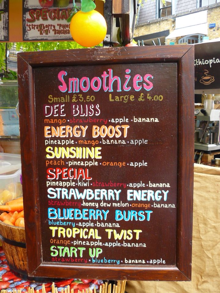 a menu for smoothies and juices is displayed on a wooden sign in front of a store