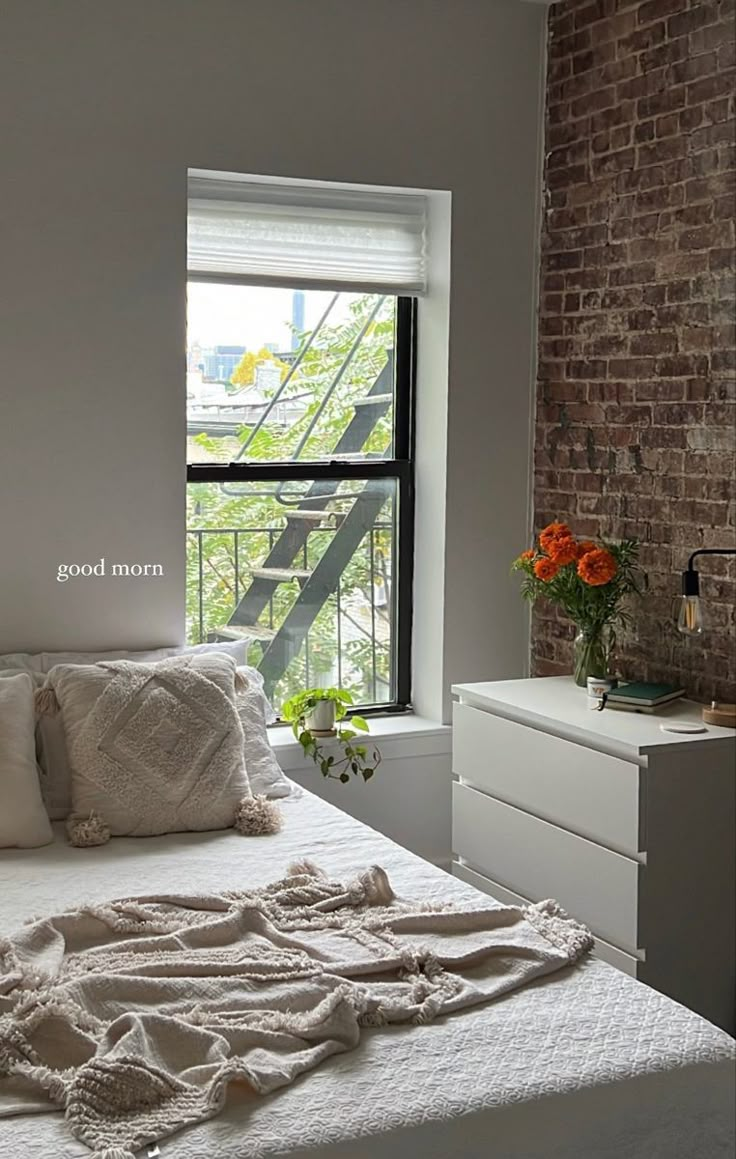 a white bed sitting next to a window in a room with brick walls and windows