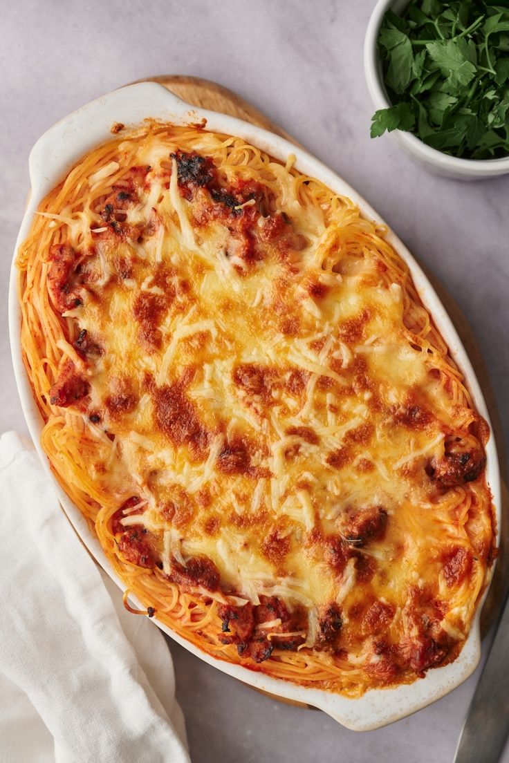 a casserole dish with meat and cheese on it next to a bowl of greens