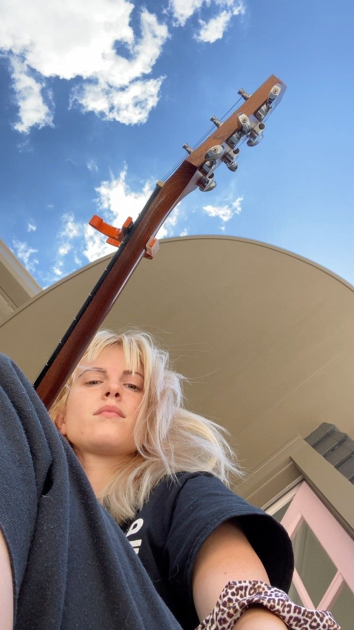 a woman is holding a guitar in front of her face and looking up at the sky