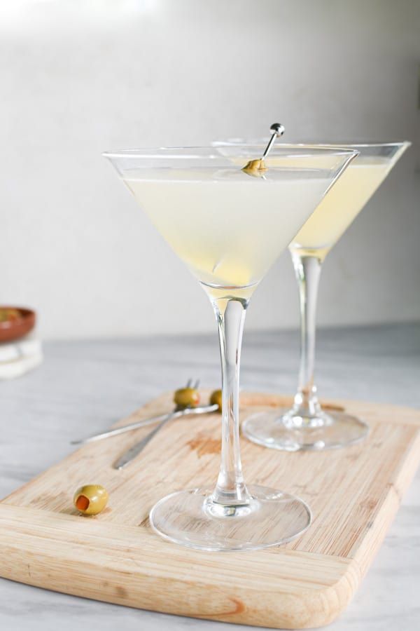 two martini glasses on a cutting board with olives