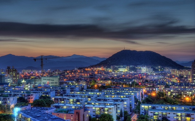 the city is lit up at night with mountains in the background