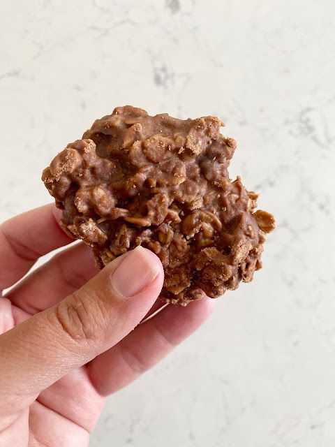 a hand holding up a chocolate cookie on a marble counter top, with the bite taken out