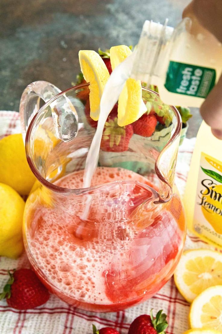 a pitcher filled with liquid next to lemons and strawberries