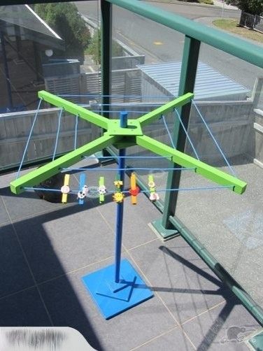 a green and blue sculpture on top of a metal pole next to a glass wall