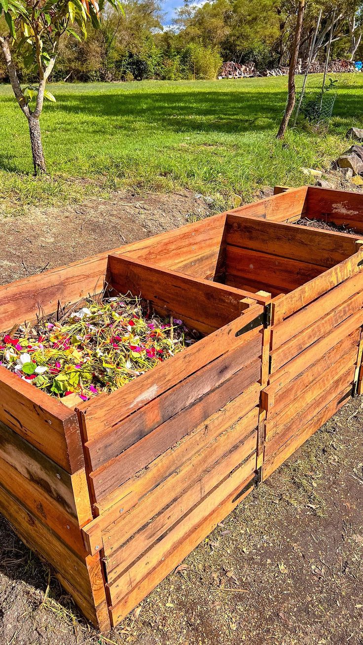 a wooden planter filled with lots of flowers on top of a dirt ground next to a field