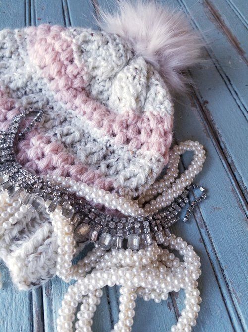 a knitted hat with pearls and beads on top of blue wooden planks next to an earring