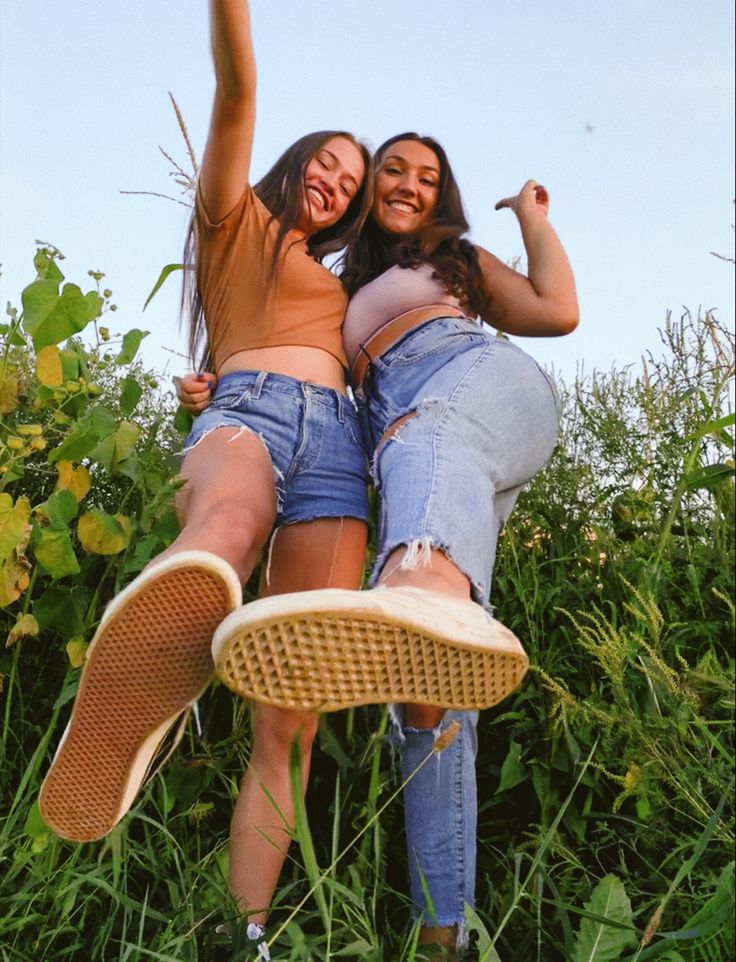 two young women are posing in the grass