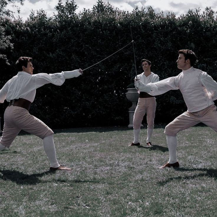 two men in white shirts and pink pants are practicing martial moves on grass with trees in the background