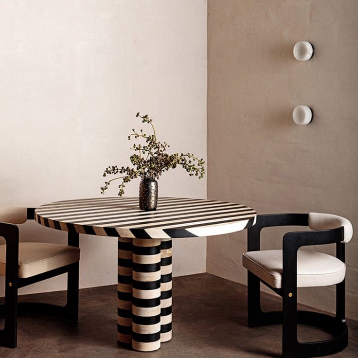 a table with two chairs and a vase on it next to a wall mounted light