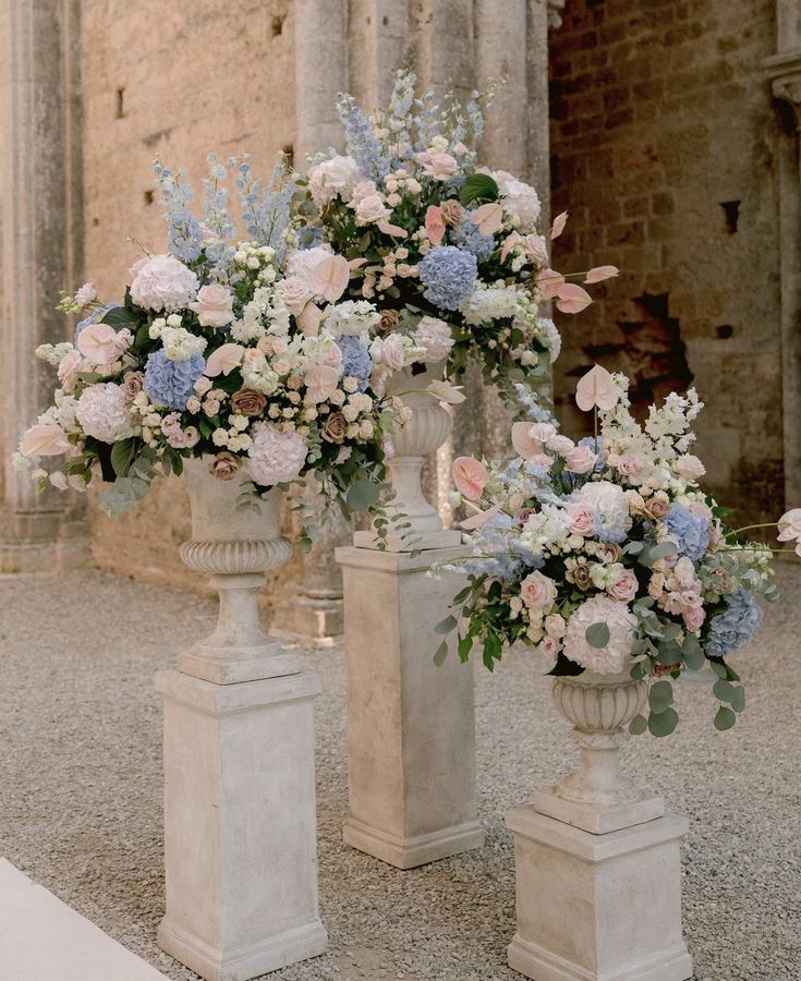 three white vases filled with flowers sitting on top of a stone floor next to each other