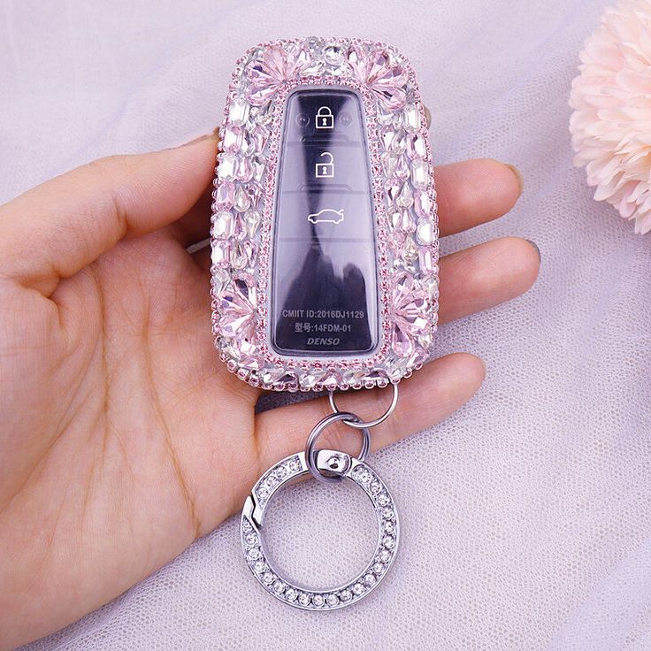 a hand holding a cell phone with a keychain attached to the back of it