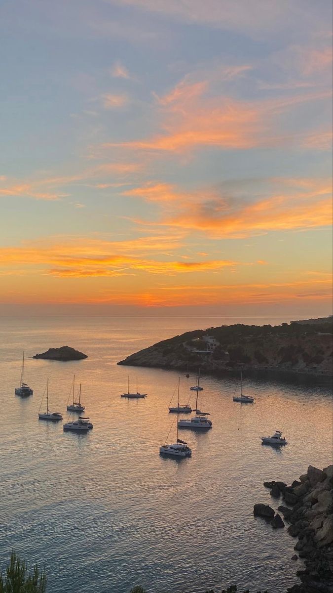 several sailboats floating in the ocean at sunset