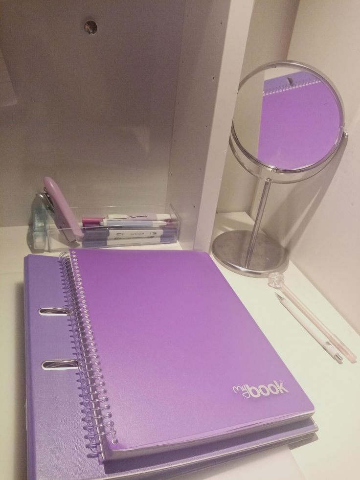 a purple notebook sitting on top of a table next to a pen and glass container