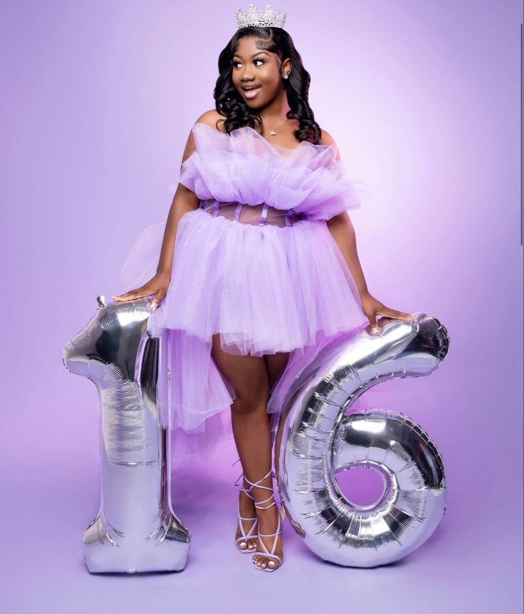 a woman in a purple dress standing next to a giant number six balloon with a tiara on her head