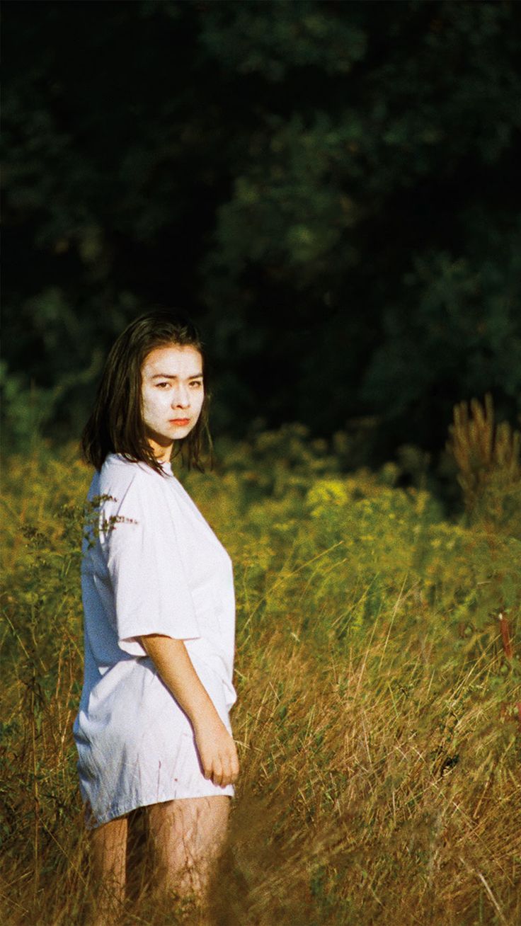 a woman standing in tall grass with her face painted white