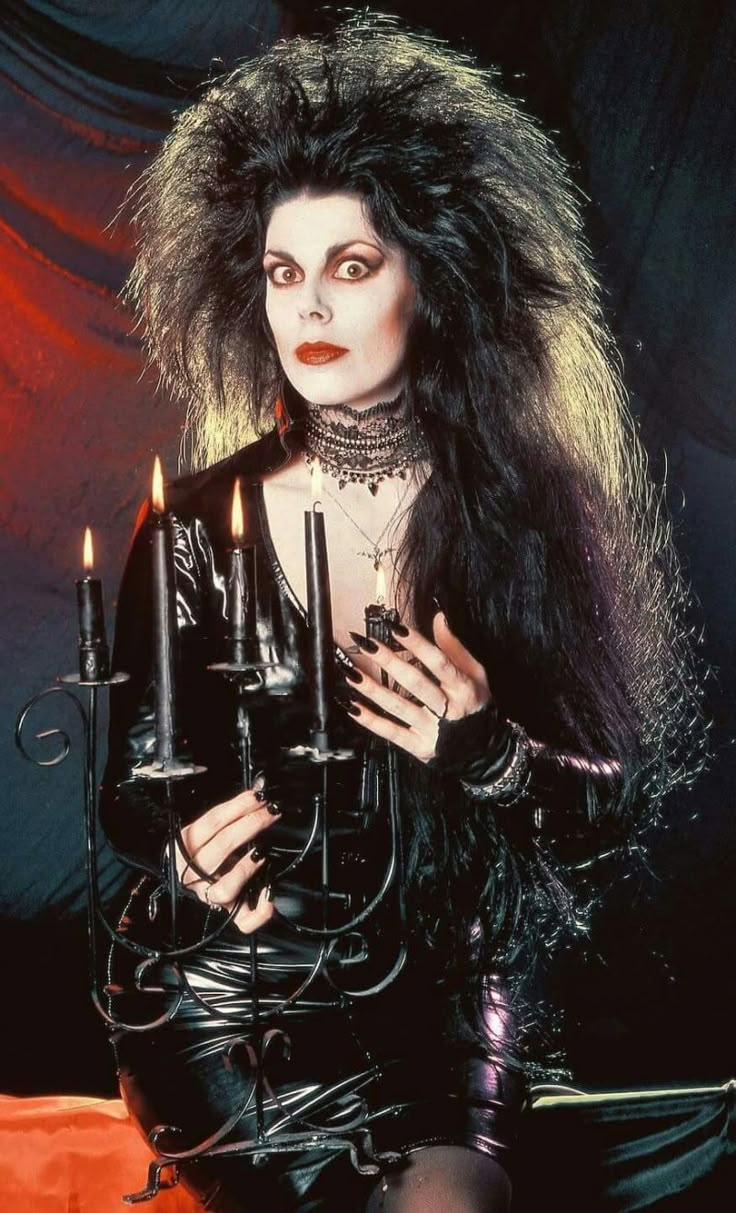 a woman with long hair holding candles in her hands and wearing black leather clothes,